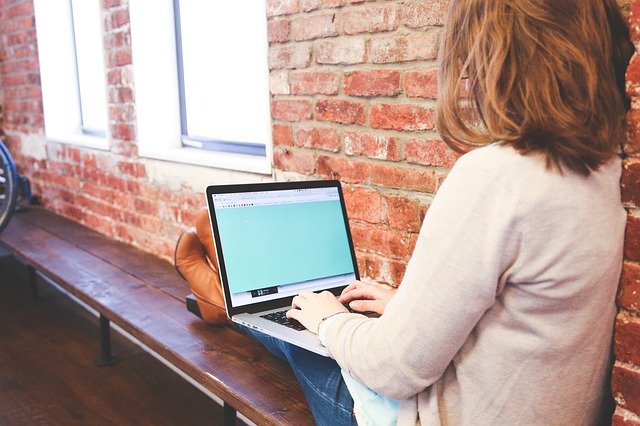 Žena sedí pri okne a píše na počítači